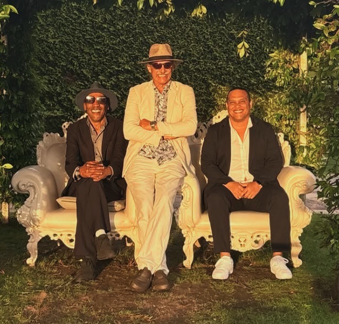 Los Três Amigos — trio sentado num sofá branco no jardim